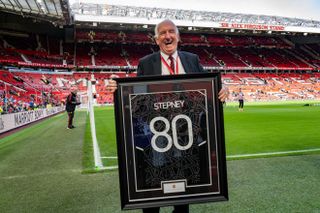 Former Manchester United goalkeeper Alex Stepney poses with a framed shirt to mark his 80th birthday at Old Trafford in October 2022.