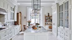 Kitchen with white cabinets and built-in drawers, island with marble countertop and pendant lights with vintage dresser