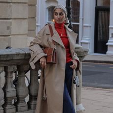 Woman wears trench coat, red roll neck, blue jeans