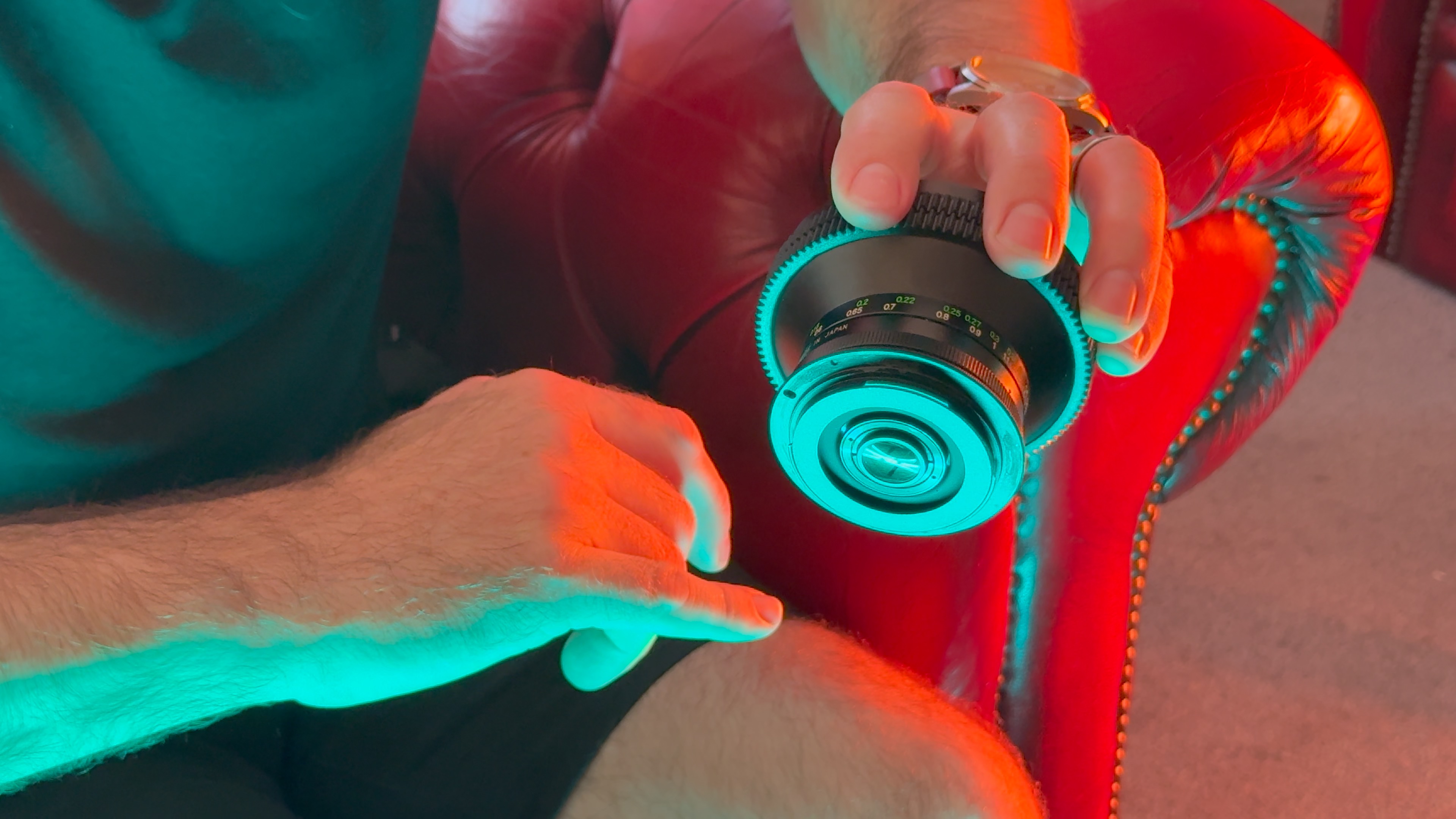 A person handling a camera lens lit by a red light