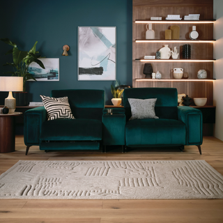 a teal velvet cinema-stye sofa in a living room with lit up shelves behind