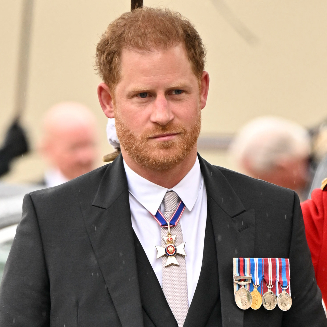 Prince Harry is a man with ginger hair, and a slight smirk on his face, wearing a black suit with military medals attached to the lapel