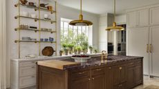 A kitchen with white cabinetry, a wooden island with a red marble countertop, and brass hardware and pendant lights