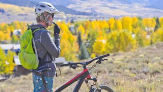 Woman drinking from a hydration pack next to a mountain bike in the hills