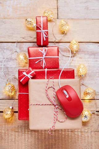 High angle view of Christmas gifts, red computer mouse and string lights on wooden table, online shopping