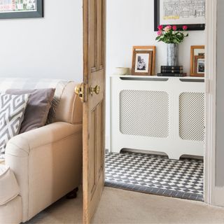 Door from a living room opening up to a hallway with checkered tiled floor and a white radiator cover