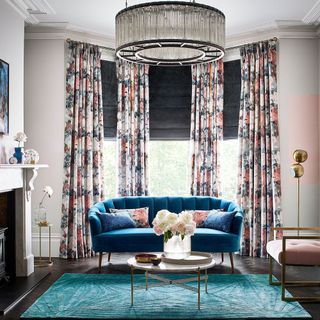 living room with bay window covered by full length pink floral curtains, a rich blue sofa with matching blue and floral cusions and a green rug