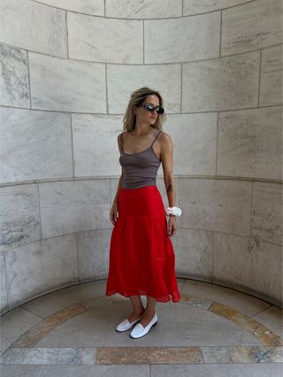 Eliza Huber wearing a red midi skirt, tan camisole, white loafers, and white scrunchie from the J.Crew x Maryam Nassir Zadeh collaboration.