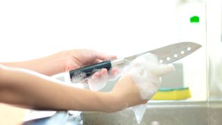 Someone cleaning a knife with soapy water and a cloth