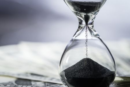 hourglass with black sand sitting on top of dollar bills