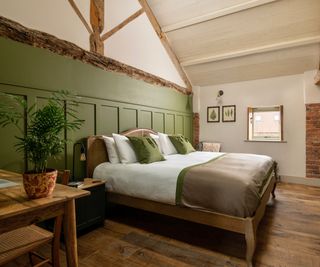 bedroom with exposed timber beams above a green panelled wall with bed in front