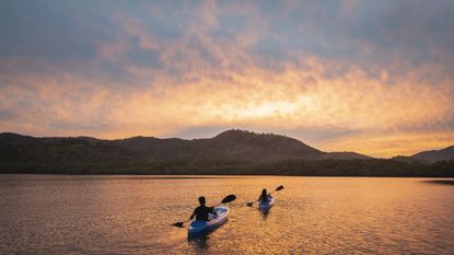 A pair of kayakers paddle into the sunset on calm waters.