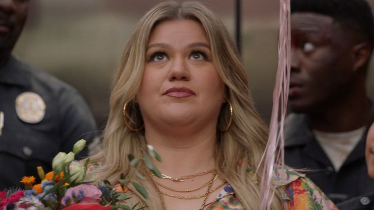 Kelly Clarkson holding flowers and baloons looking up while standing in an elevator.