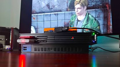 PS2 console with GBS-C upscaler connected via SCART and sitting on top with James from Silent Hill 2 on screen in backdrop.