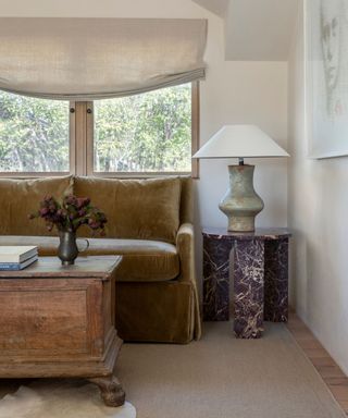 small neutral living room with a brown velvet couch and a red rosso marble side table with an antique wooden chest as the coffee table