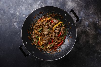 Prawn and noodle stir fry in a wok on a grey background