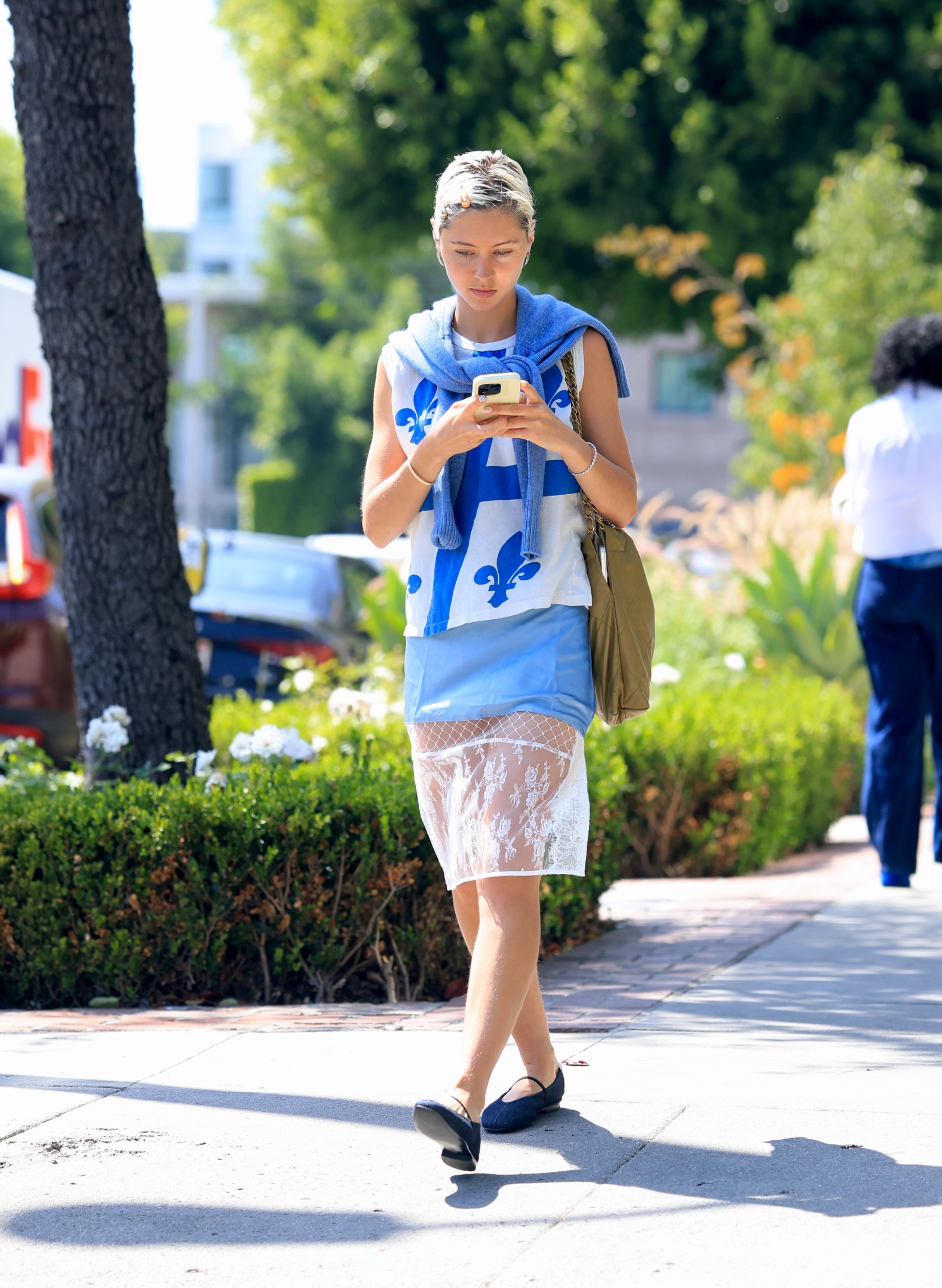 Iris Law walks down the street in L.A. wearing a sheer skirt with navy ballet flats and a longline t-shirt.