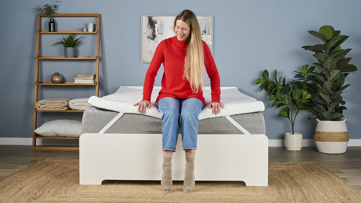 A tester sits on the foot of the Helix Dual Comfort Mattress Topper, which has been placed on a bed.