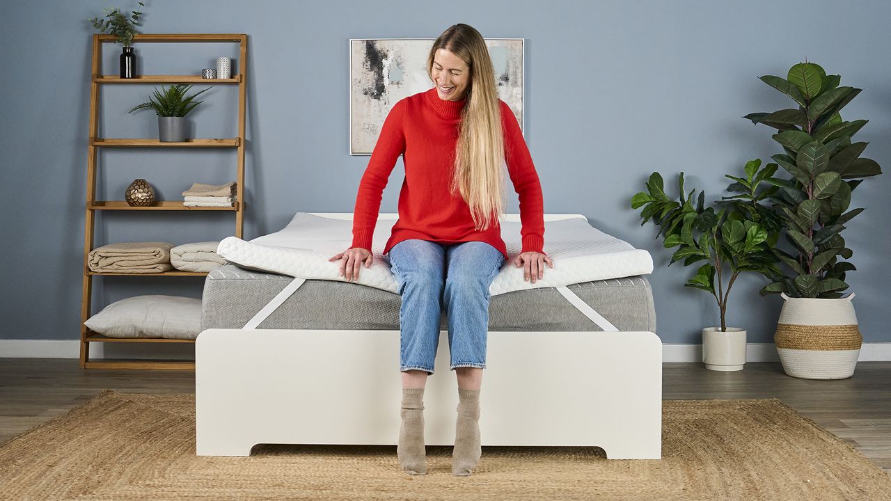 A tester sits on the foot of the Helix Dual Comfort Mattress Topper, which has been placed on a bed.