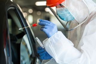 A healthcare provider administering a COVID-19 test at a drive-through.