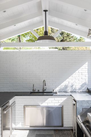 an outdoor kitchen with brick finish under a pitched roof