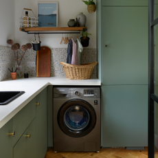 Green/blue cupboards, gold leaf island unit, large patterned tiles above the sink. Wooden dining table, with wooden slatted wall behind. Utility behind dining table and snug area behind kitchen