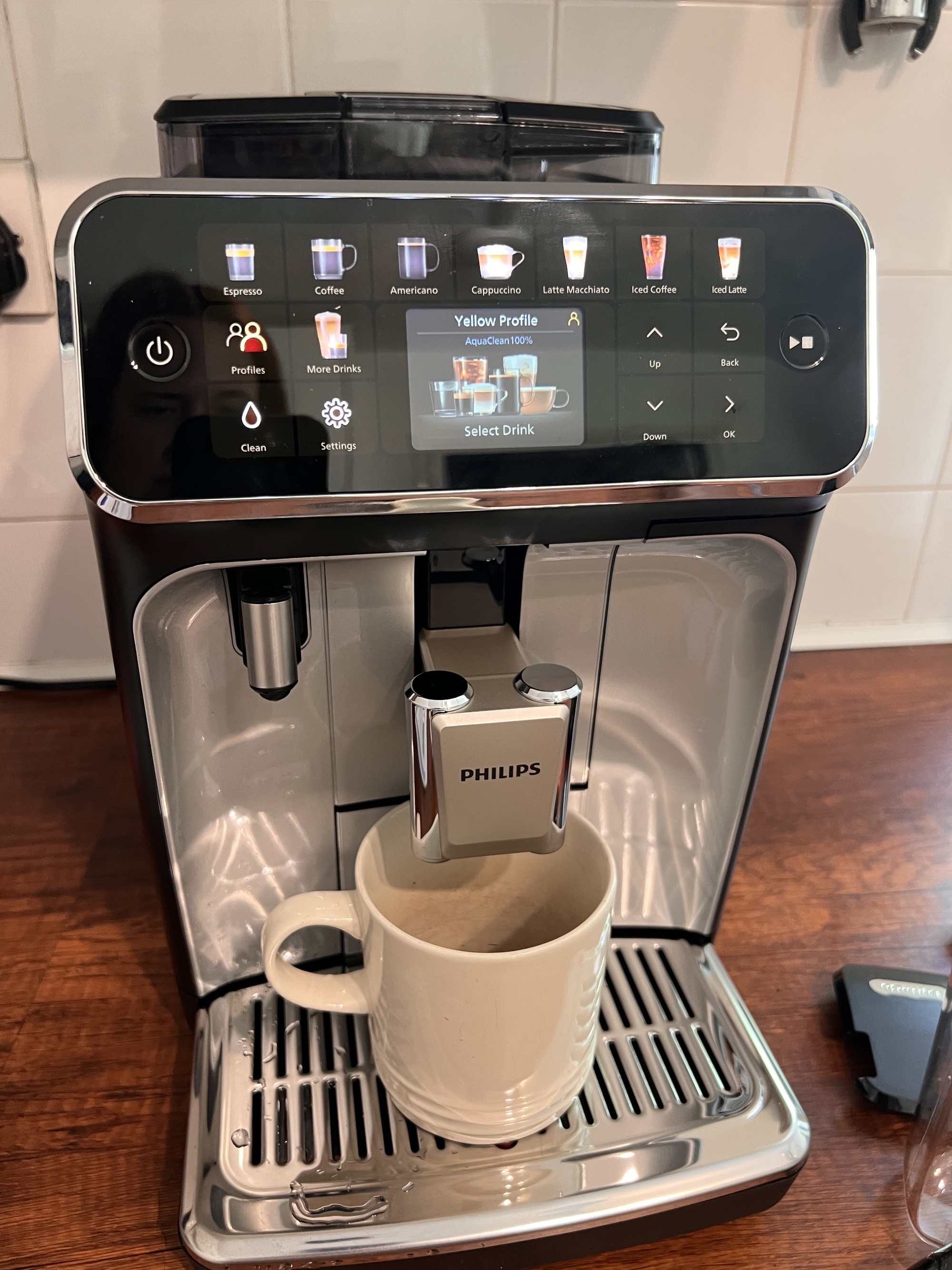 Image of the Philips Series 5500 coffee machine with a cream coffee mug under it on a wooden countertop in a white kitchen.