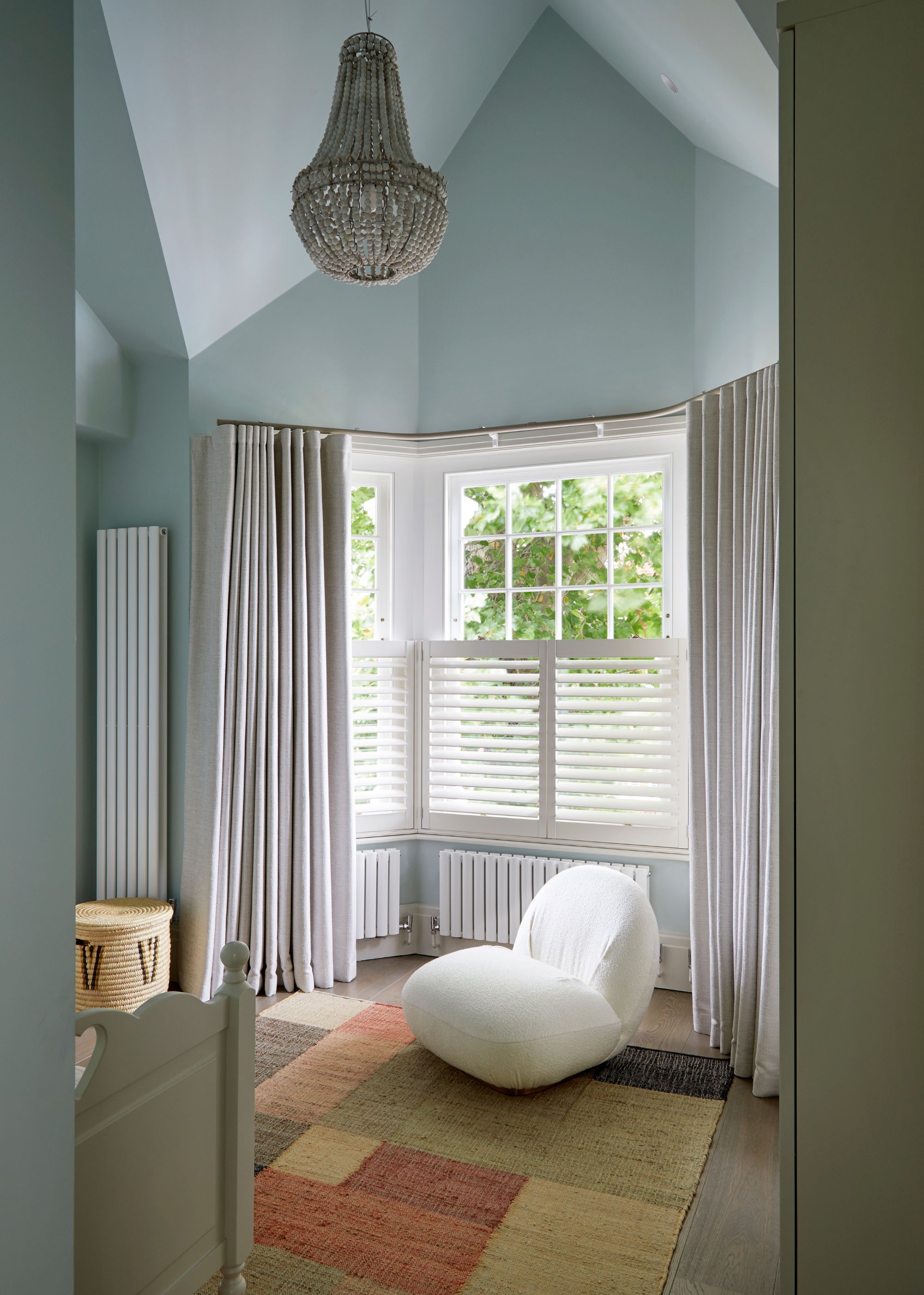 calming bedroom with light blue walls, bay window with white shutters and light gray curtains