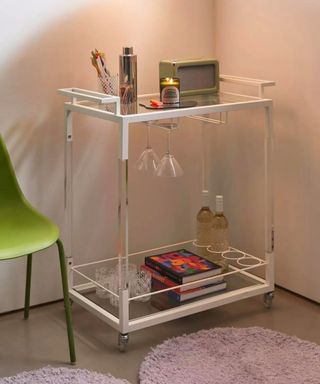 a bar cart with glasses and books on a purple rug next to a green chair