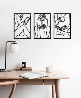 Three black wall arts with a person reading above a decorated wooden desk