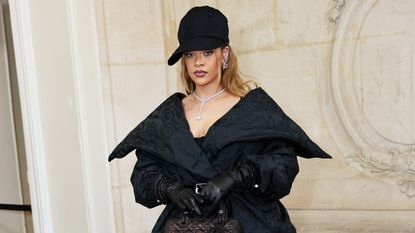 Rihanna wearing a black peplum style coat with a black cap 