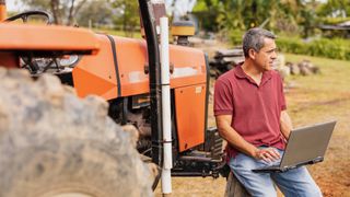A middle-aged man using a laptop while sitting on his tractor