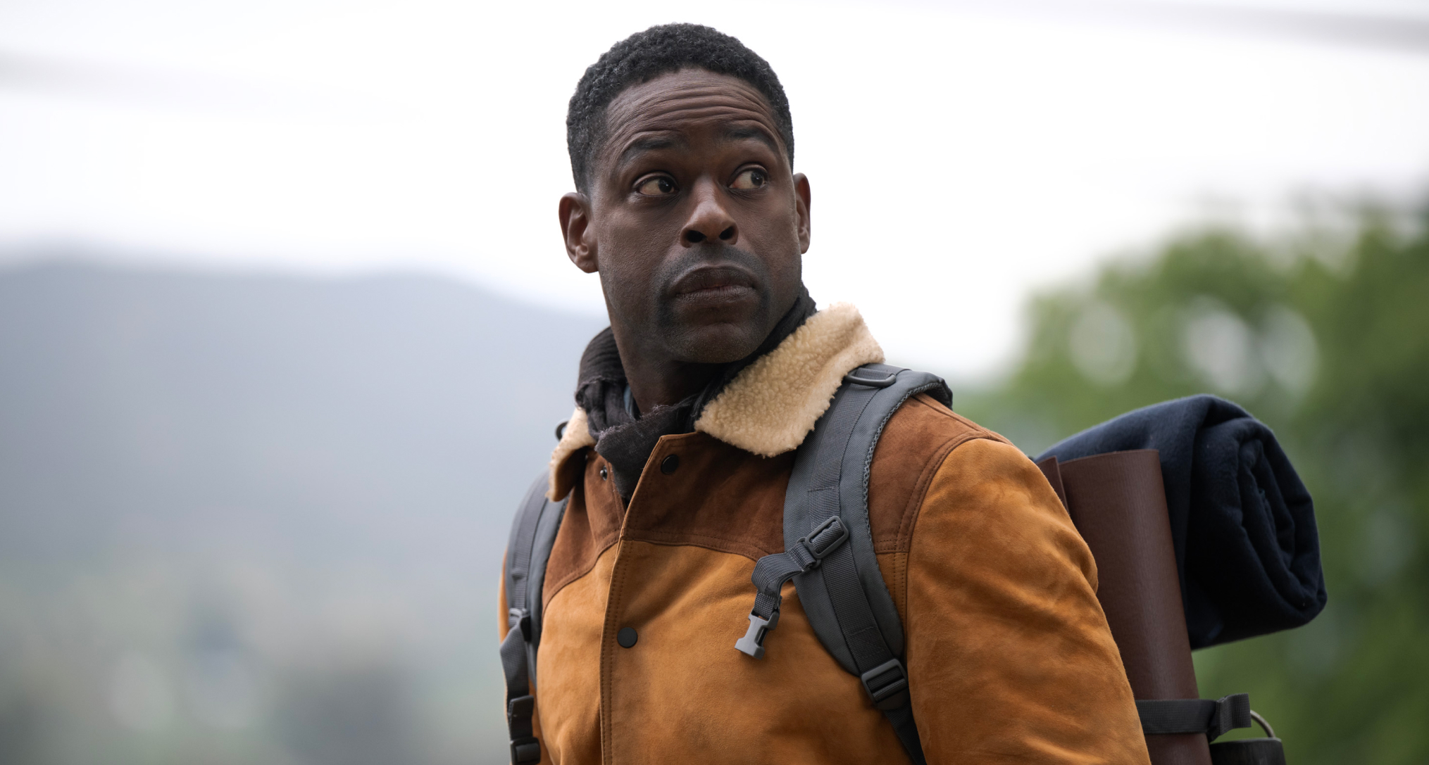 sterling k brown as xavier wearing an orange jacket and carrying camping gear on a mountain in paradise season 2
