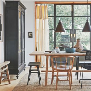 dining room with light curtains, grey dresser, grey pendant lights, retro style table and chairs, black stools, jute rug, earthenware on table