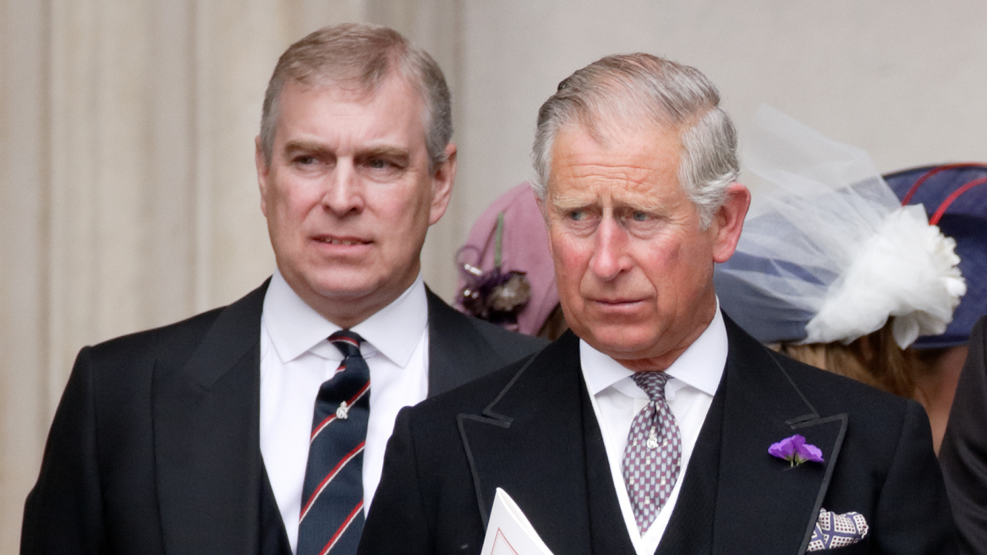 Prince Andrew wears a suit and stands behind King Charles