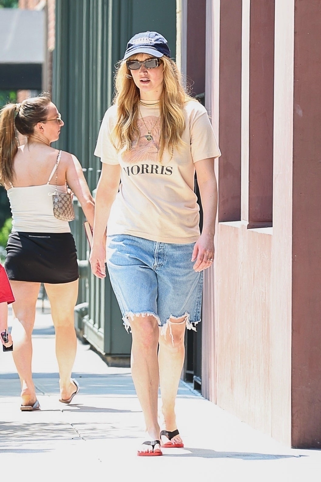 Jennifer Lawrence wearing a vintage T-shirt, jorts, The Row flip-flops, and a baseball cap
