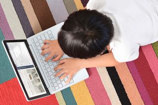 Child typing on a Microsoft Surface Laptop SE on a rug