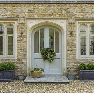 arched front door in cotswold stone extension with Christmas wreath and box plants in pots