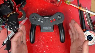 Hands at each side of modded Virtual Boy controller with Switch 2 board on red workbench.