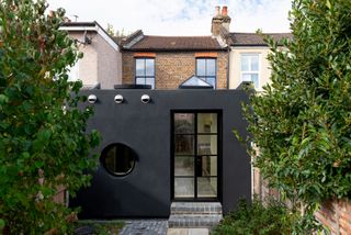 cladding on black terraced house extension in London, with small French doors and a circular window leading onto the garden