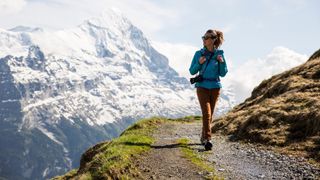 Woman walking across a ledge with snowy mountains behind