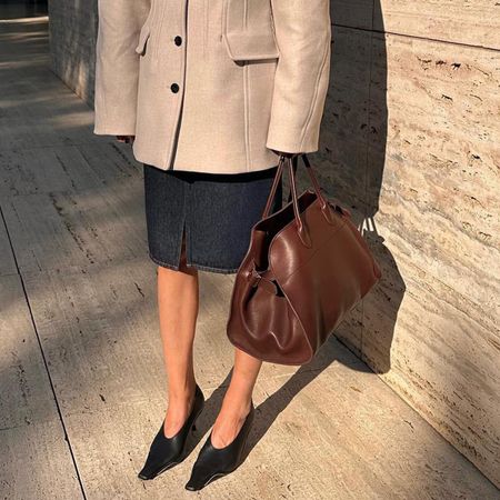 @iliridakrasniqi wearing a skirt, pumps, a blazer, and a brown The Row Margaux bag.