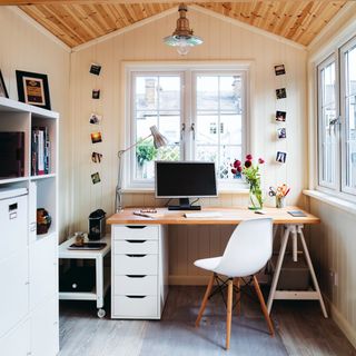 White garden office, panelled walls, wood ceiling, desk, with filing cabinet, white eames chai
