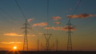 Two rows of power lines are seen in a orange and blue sunrise.