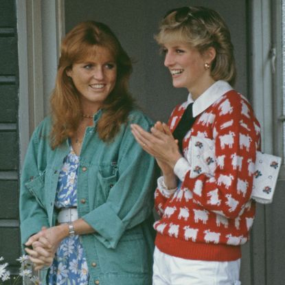 Sarah Ferguson wearing a green shirt and blue floral dress smiling at Princess Diana, who is wearing a red sheep sweater