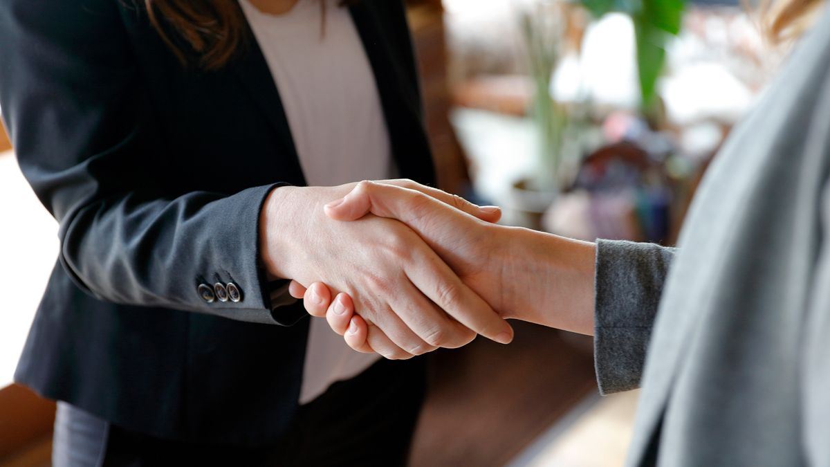 Two female business people shaking hands in suits.