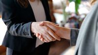 Two female business people shaking hands in suits.