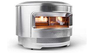 Solo Stove pizza oven in stainless steel with fire inside, shown on white background.
