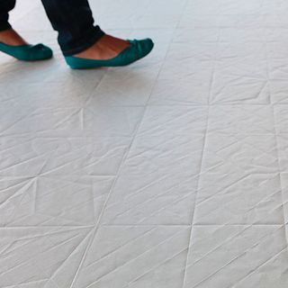 White porcelain floor tiles which have the textural appearance of folded and unfolded paper, with a womens feet shown walking on them