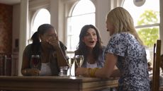 Three girlfriends laugh and talk at a cafe while drinking wine. 